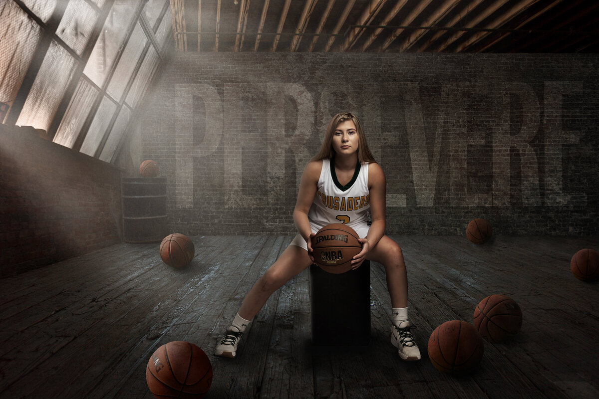 A basketball player from Catholic Memorial High School poses in a shadowy warehouse wearing her uniform for her senior portraits.