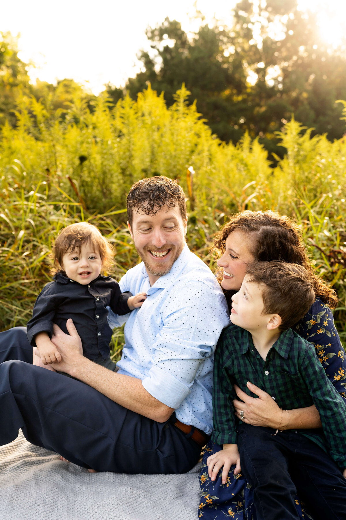 Parents with two young sons sitting in field and smiling at each other during a family portrait session in Atlanta
