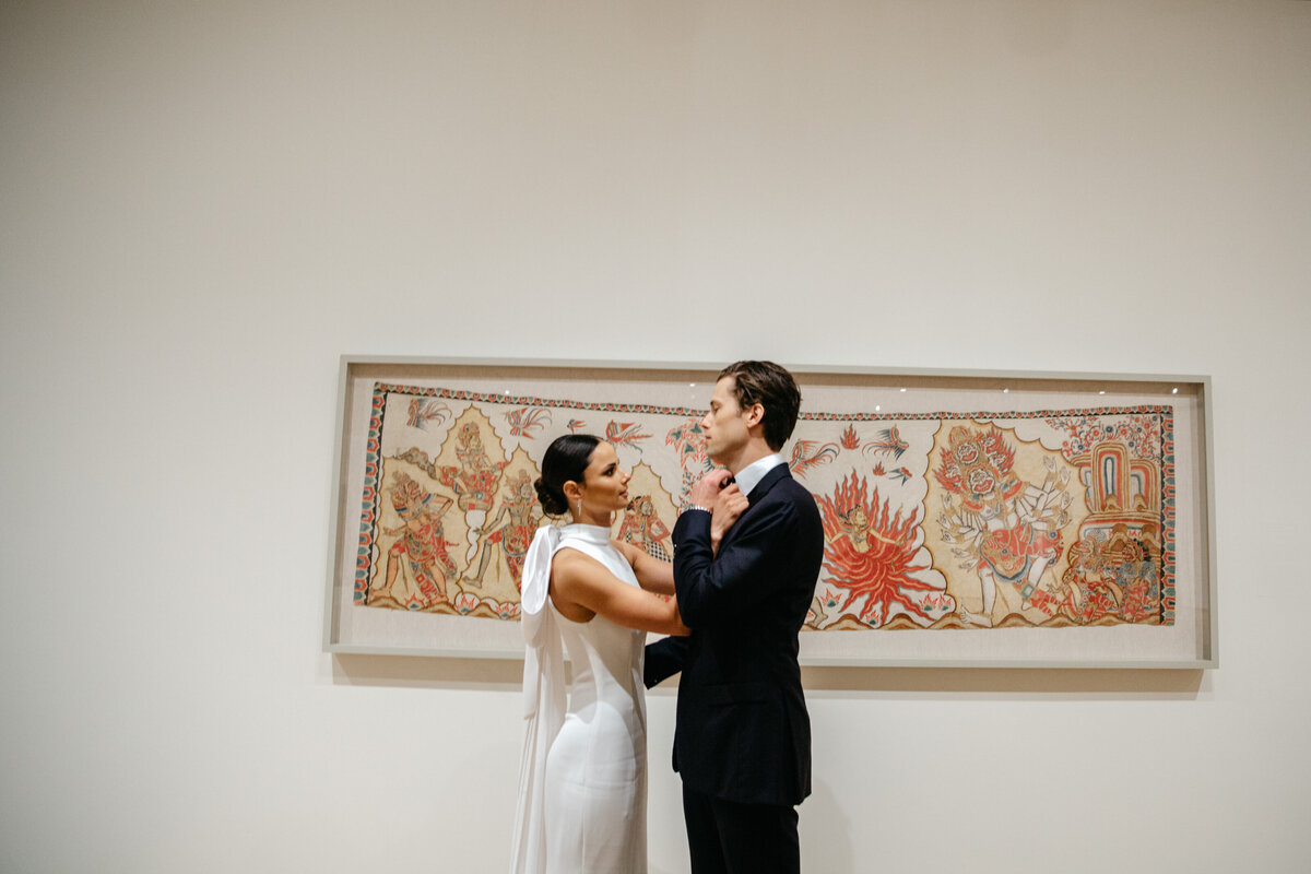 Bride adjusting groom's bowtie while standing in front of framed art at the Chicago Art Institute