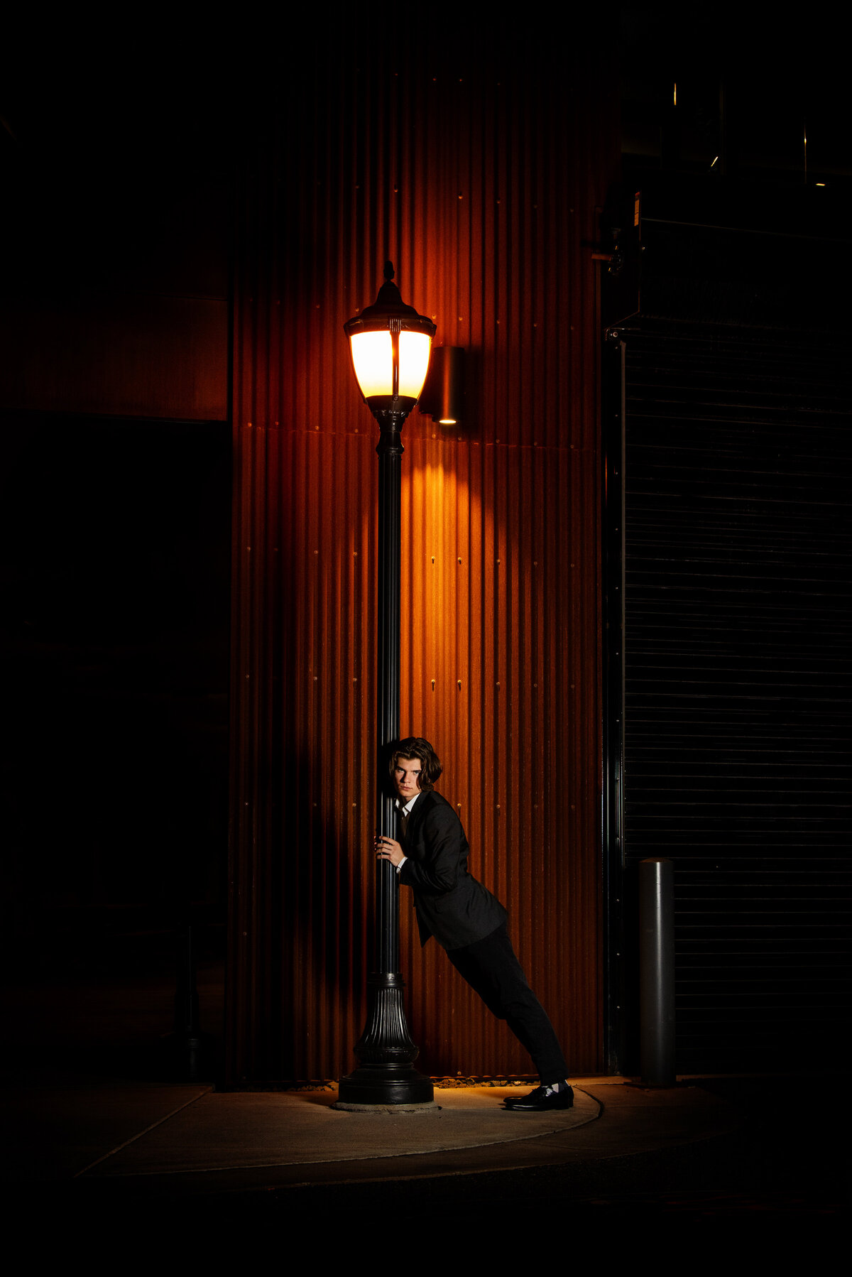 senior photo of boy in black suit leaning against  lamppost at night