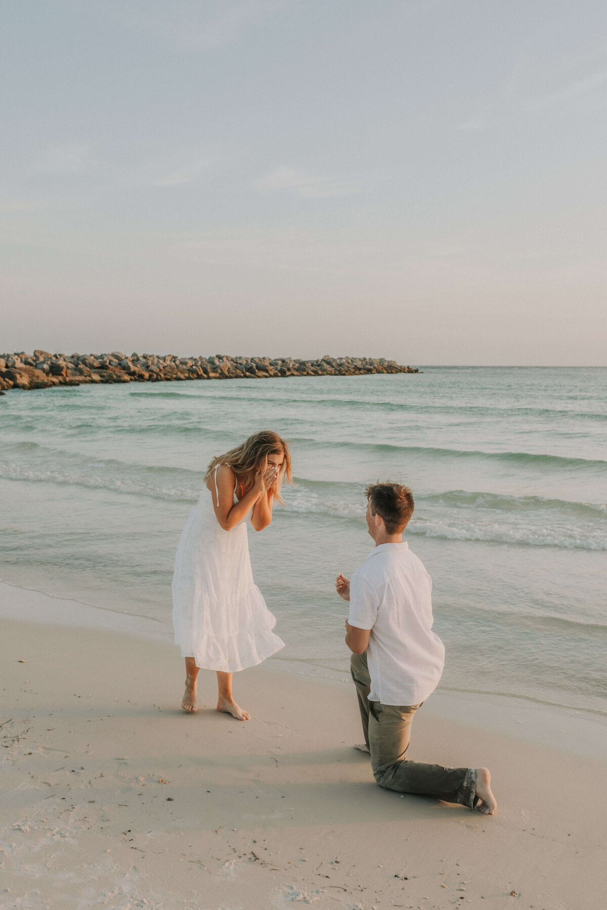 young man kneels on knee, popping the question to his new bride in PCB Fl.  Taken by Brittney Stanley of Be Seen Photos