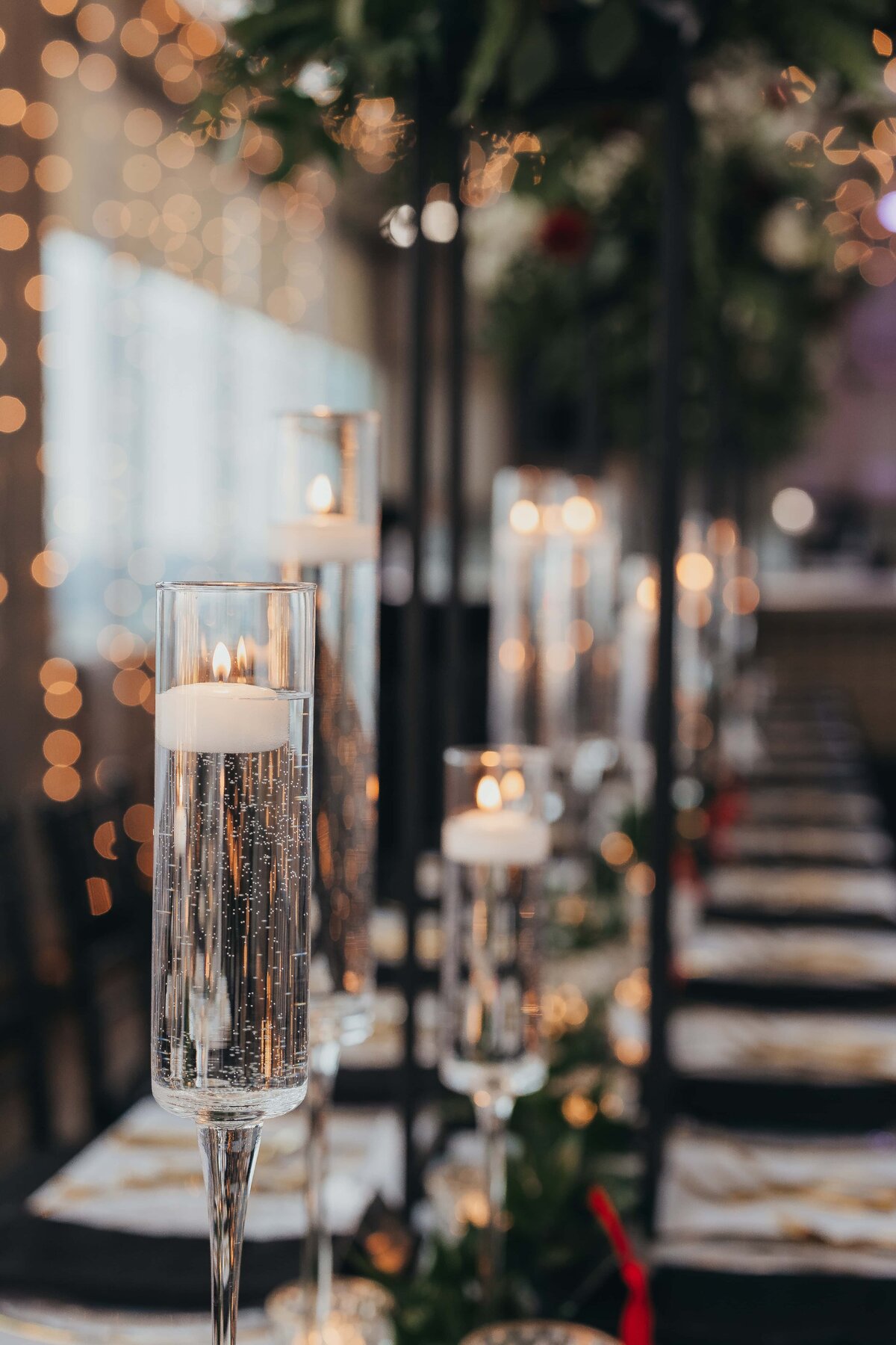 Elegant table setting with tall candle holders and lit candles, soft bokeh lights in the background at a park farm winery wedding, creating a festive atmosphere.