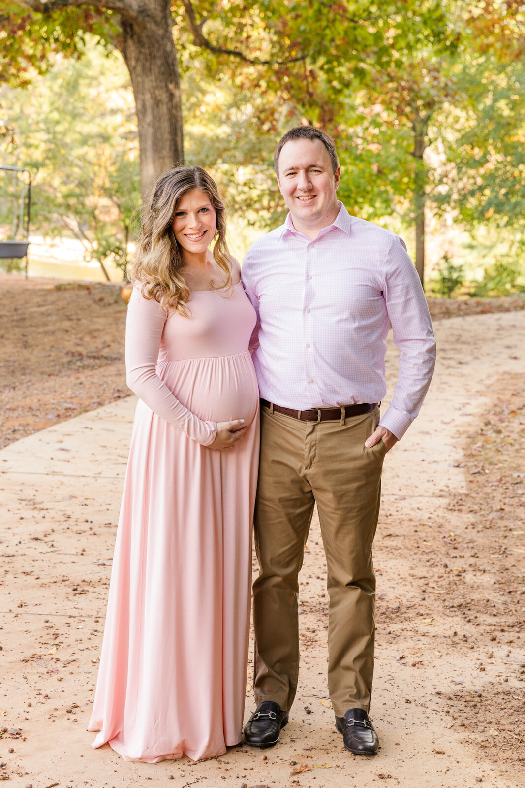 Pregnant couple with pink long dress standing on a park path in Atlanta GA