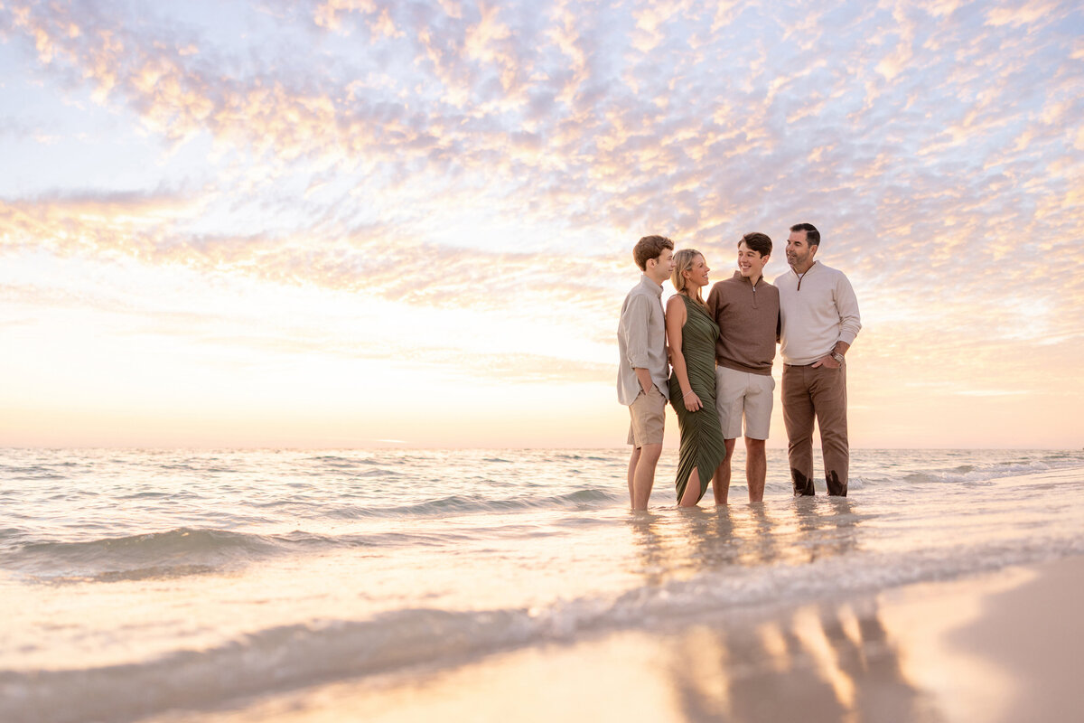 A family of four standing in shallow water at the beach