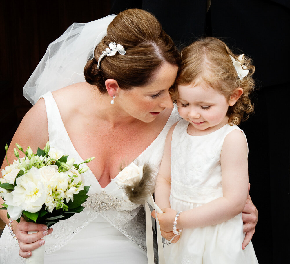 bride wearing a v neck wedding dress and hair piece hugging small flower girl