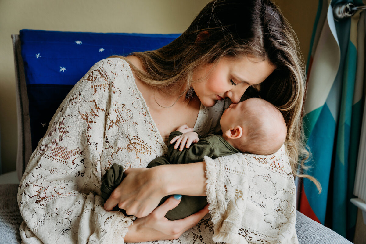 Newborn Photographer, a woman sits and holds baby while leaning in nose-to-nose tenderly