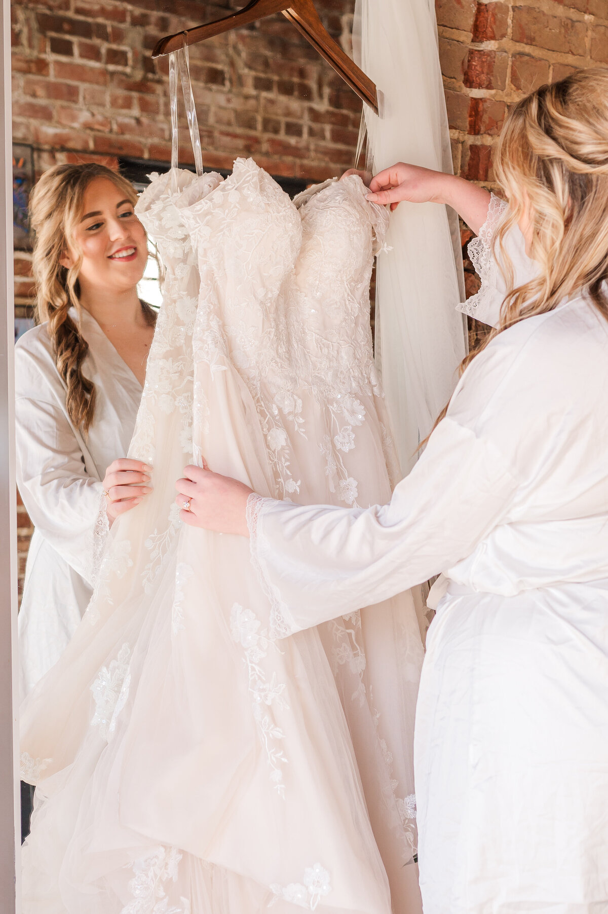 A smiling bride getting ready with her wedding dress in her hand on her wedding day in Oxford enjoying her Raleigh wedding photography by JoLynn Photography