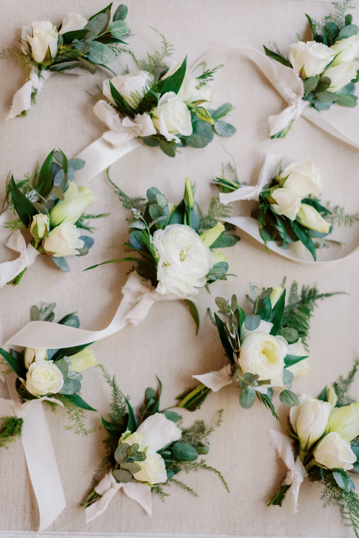 A collection of Boutonnières for the groom and groomsmen. All a collection of white flowers and greenery.