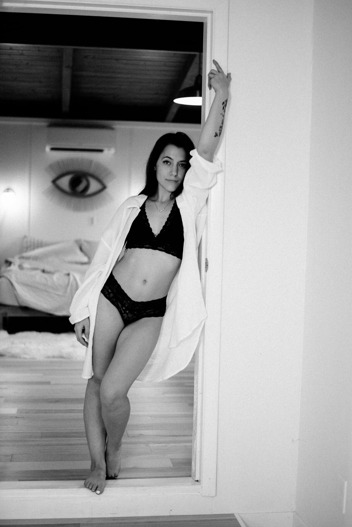 Woman in lingerie and oversized men's white tee leans in doorway.