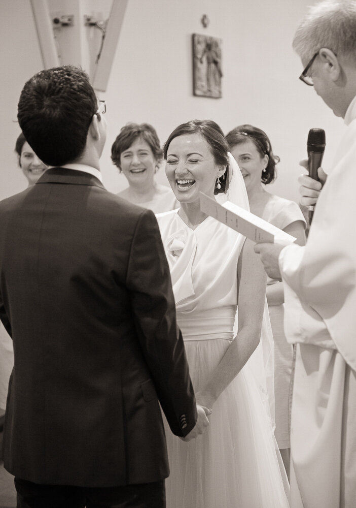 bride wearing a tulle and satin a-line wedding dress laughing while exchanging vows with her groom in Curaheen church