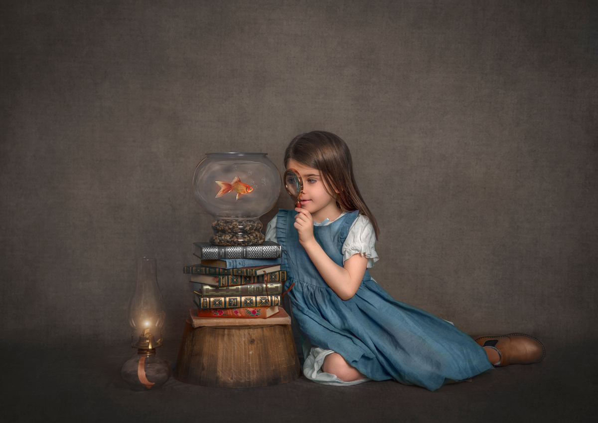 A young girl in a basic blue dress observes a goldfish througha magnifying glass. Photo taken by Sonia Gourlie.