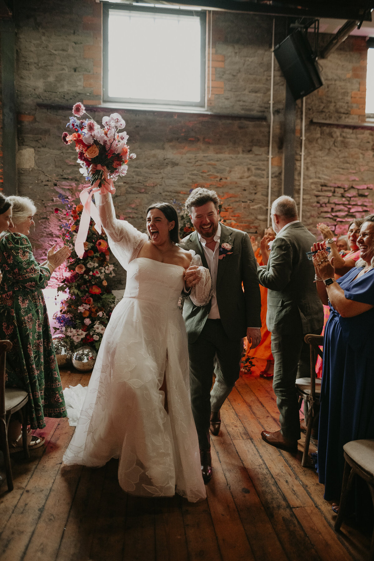 Bride and groom smile as they walk back up the aisle after their celebrant led ceremony at Paintworks in Bristol. 