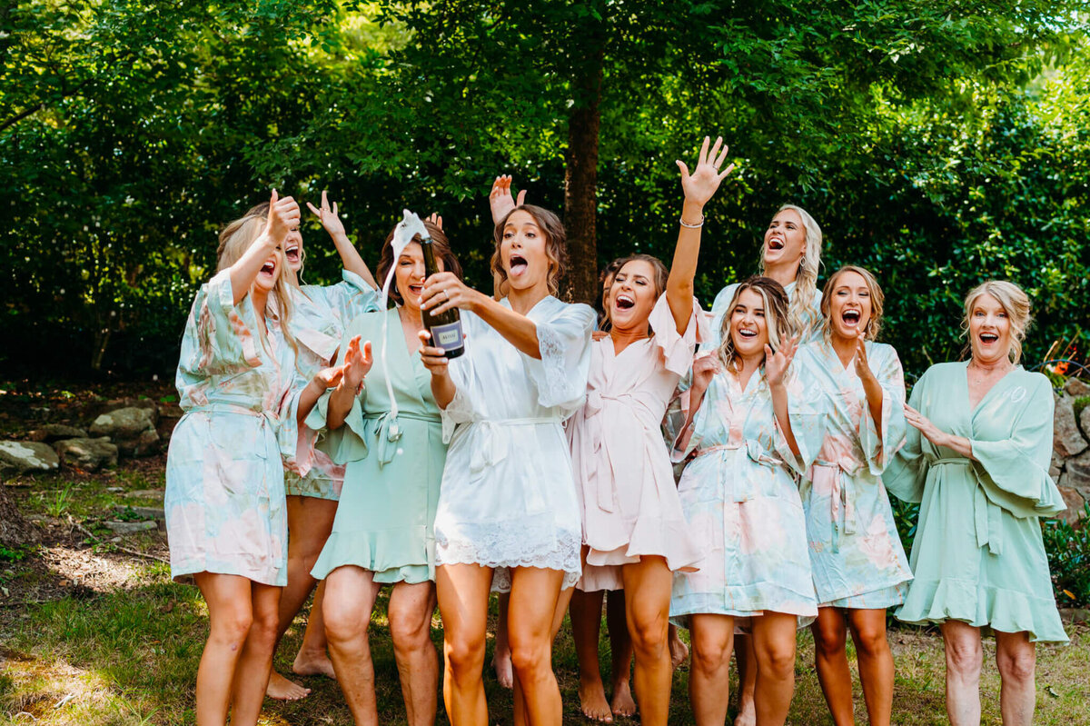 Photo of bridesmaids and robes popping a bottle of champagne and cheering