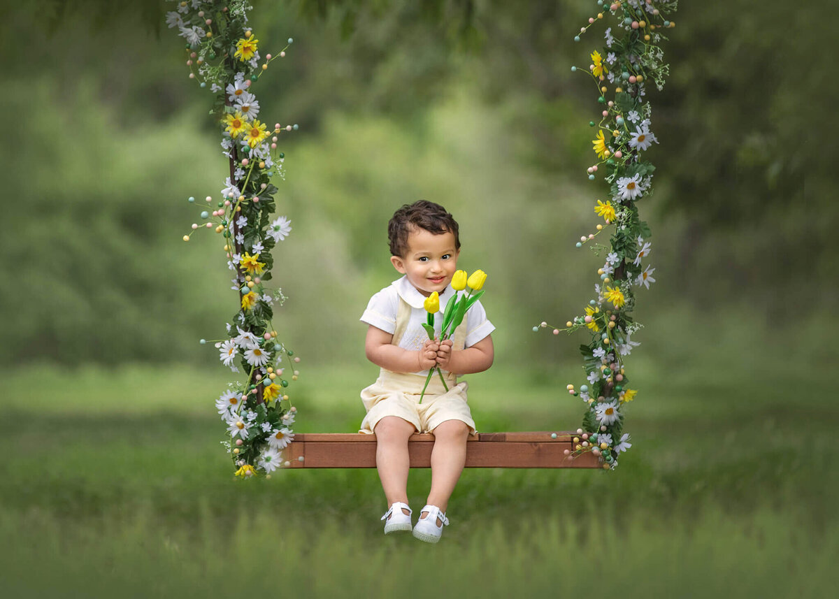 Little boy sitting in a swing with flowers in Lake Balboa Park by Los Angeles Children’s Photographer