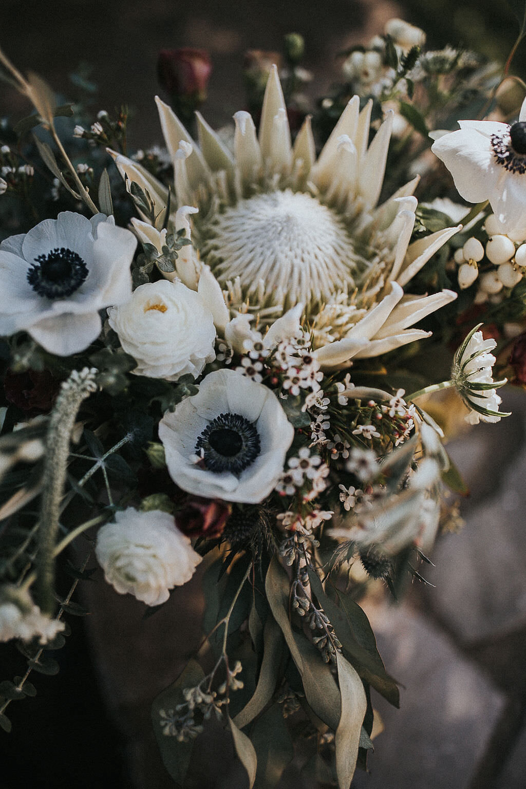bridal bouquet white white anemone, white king protea, wax flower, ranunculus, and snowberry