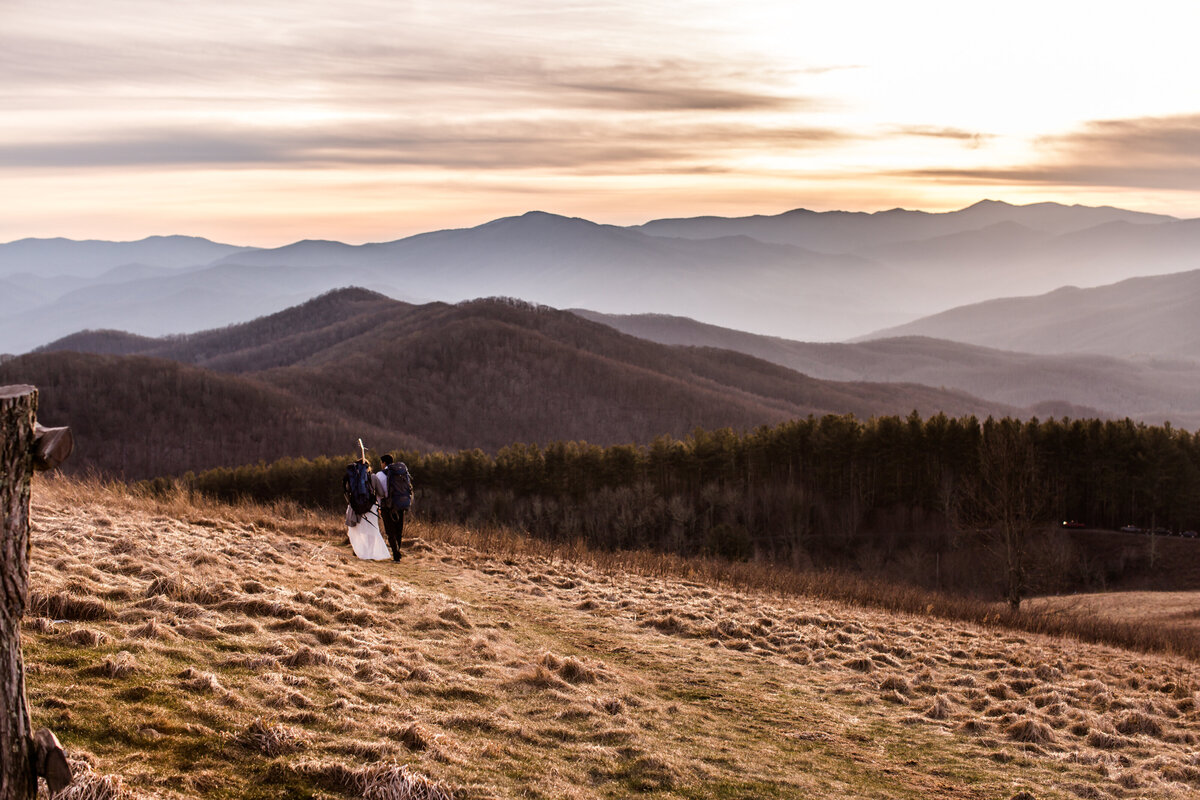 Bride and groom walking away with backpacks on into the mountains