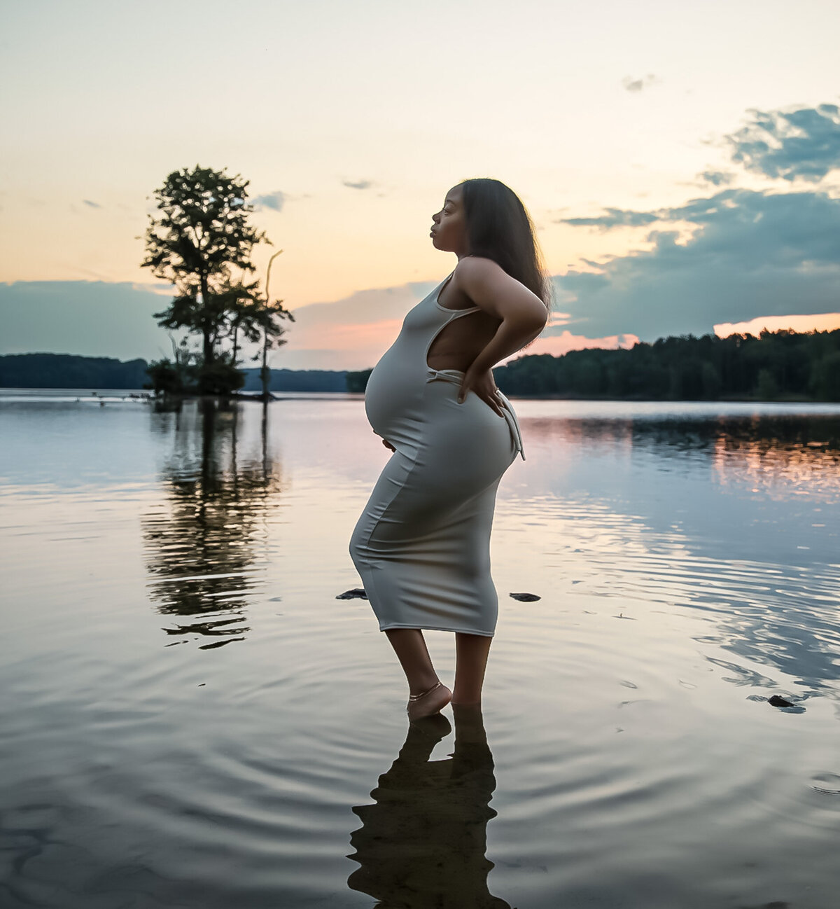 A pregnant mother stands in Loch Raven Reservoir with her beautiful baby bump at sunset