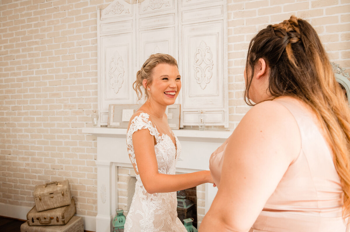 Maid of honor holding brides hand while she is getting her  dress put on
