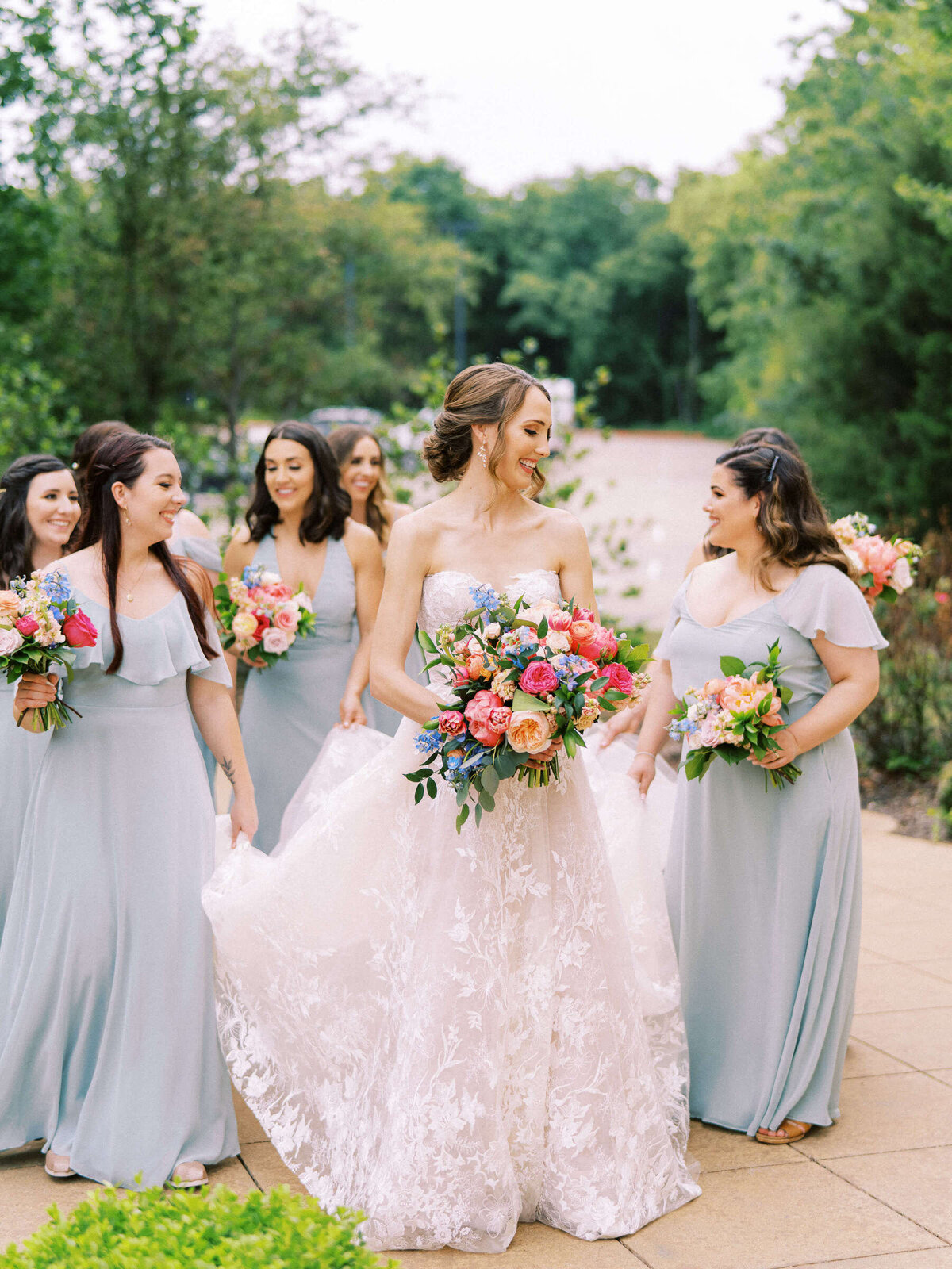 Bridal party in aqua dresses walk with bride wearing Monique Lhuillier gown and hold colorful bouquets