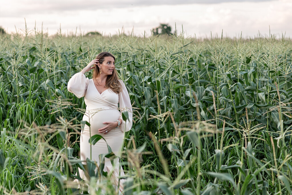 Pregnant woman in white dress standing in corn field at summer maternity sunset session | Sharon Leger Photography | CT Newborn & Family Photographer | Canton, Connecticut