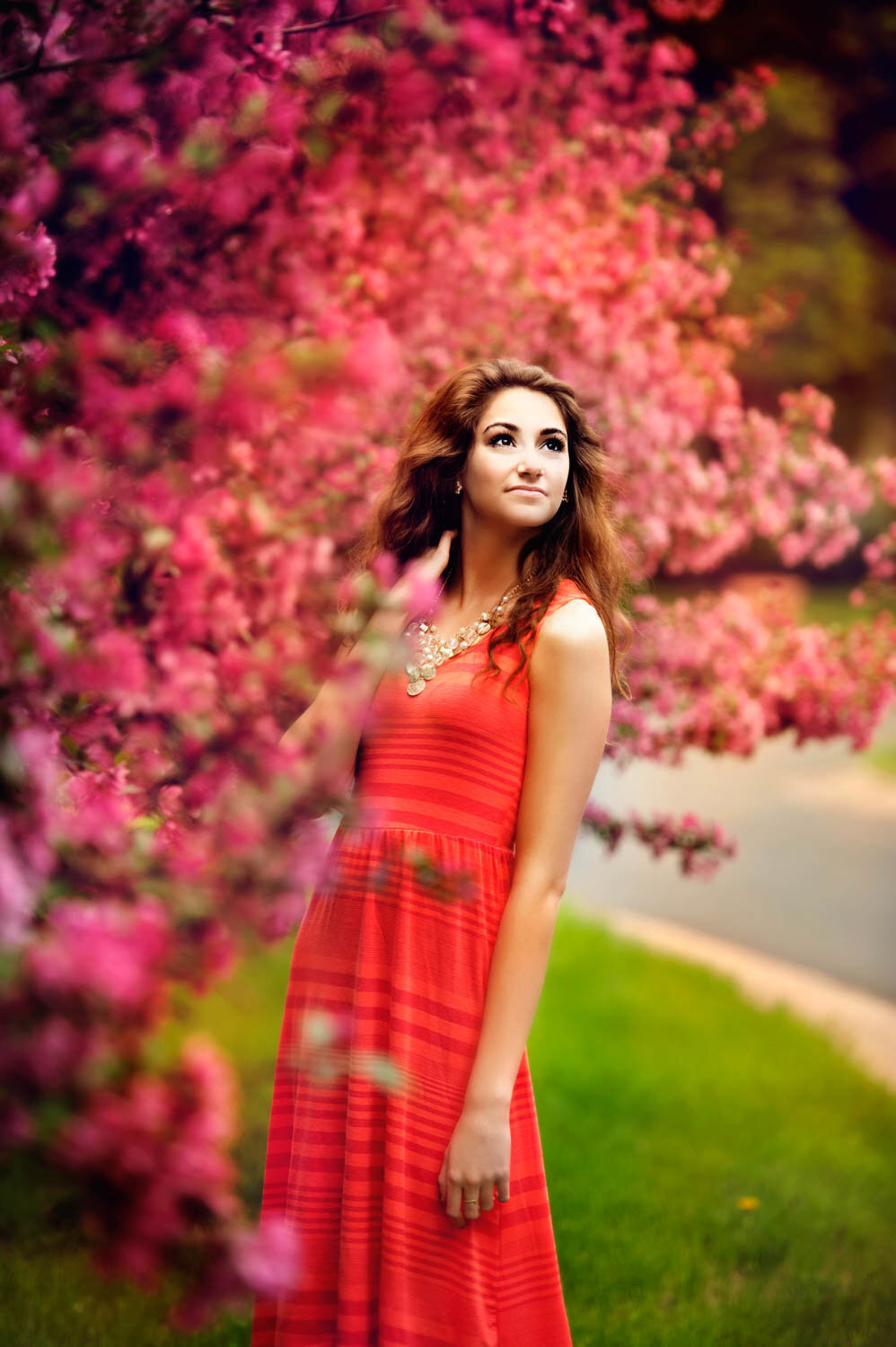 high school senior photo of girl in orange dress with pink blossoms in spring