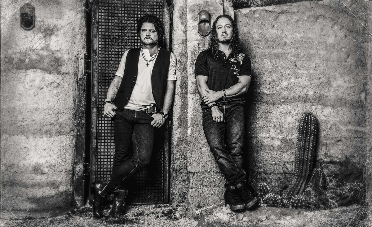 Musical duo portrait Radiofix leaning against old stone wall black and white