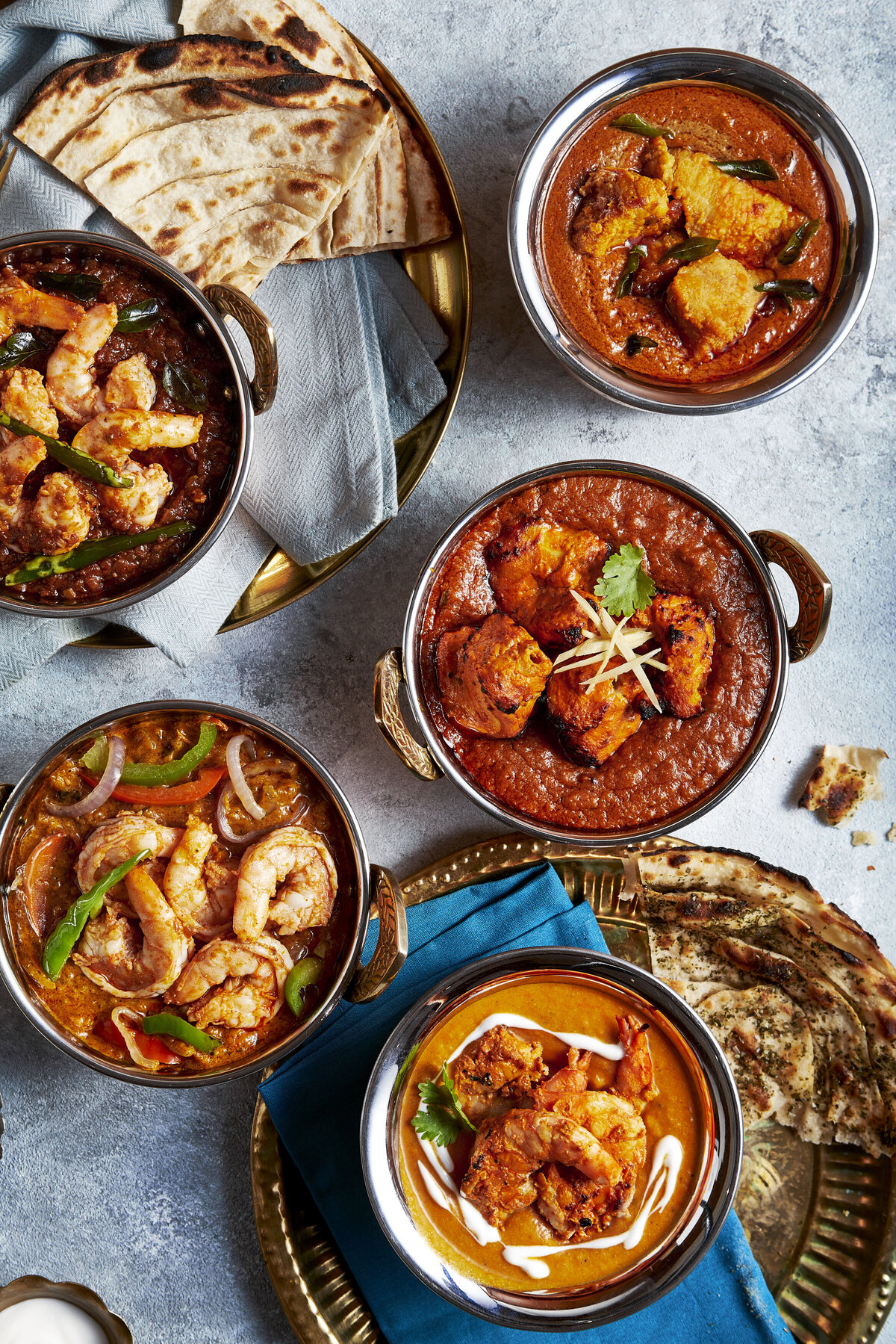 A table with a few bowls of seafood curry and a few slices of naan bread