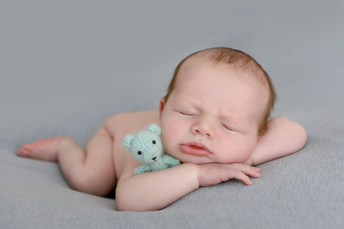 newborn-boy-sleeping-with-his-teddy-on-his-tummy-whilde-doing-his-newborn-photo-shoot