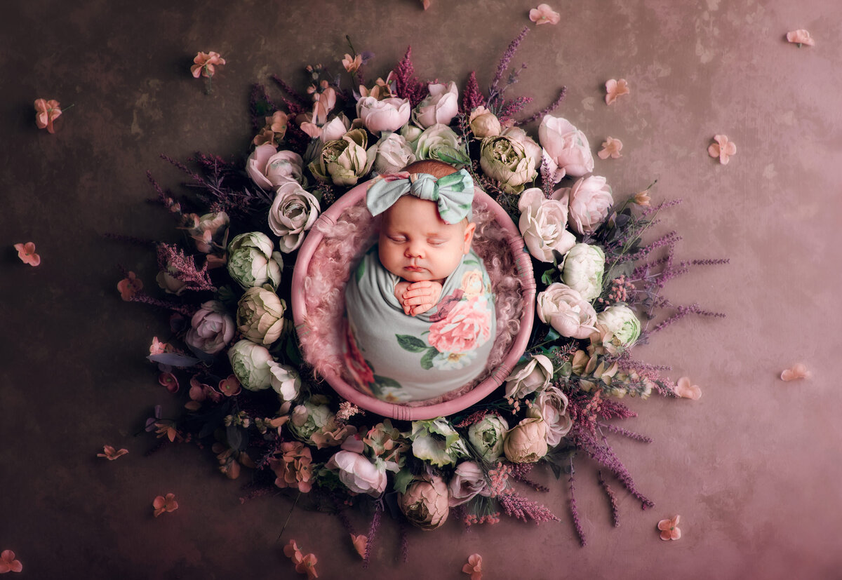 Portrait of newborn girl in the center of a floral wreath. Baby is swaddled in a floral wrap with a matching headband.