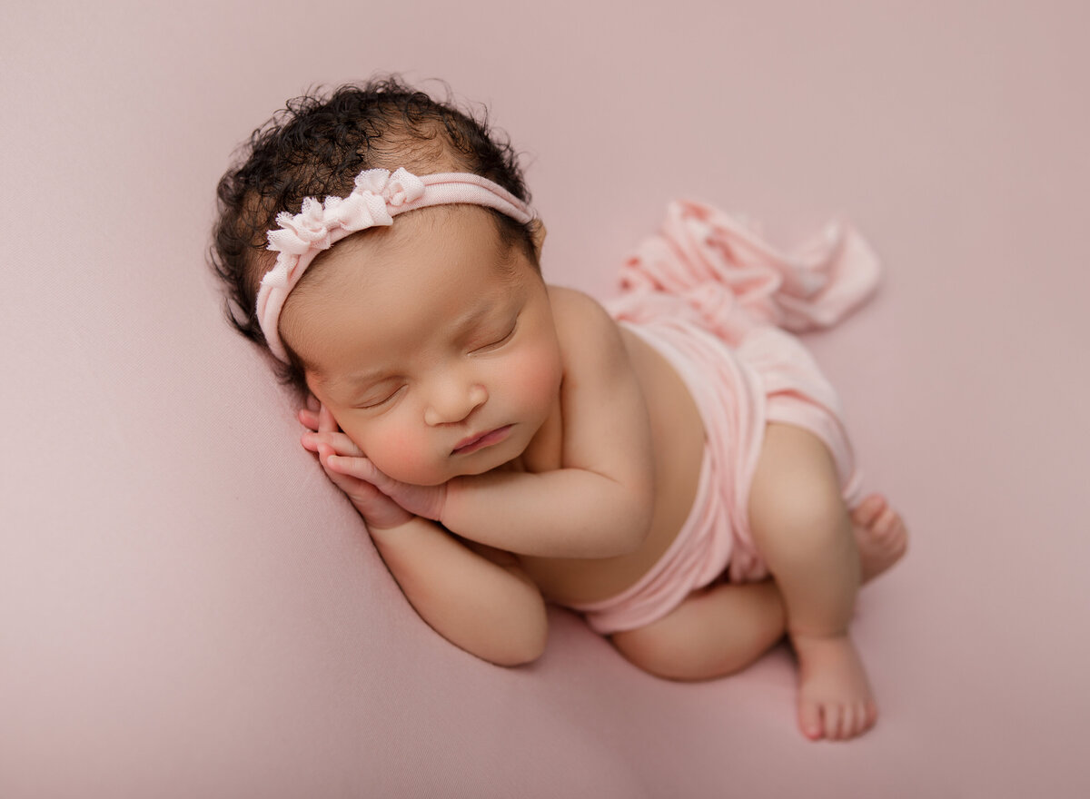 Side laying studio newborn table pose on a pink backdrop