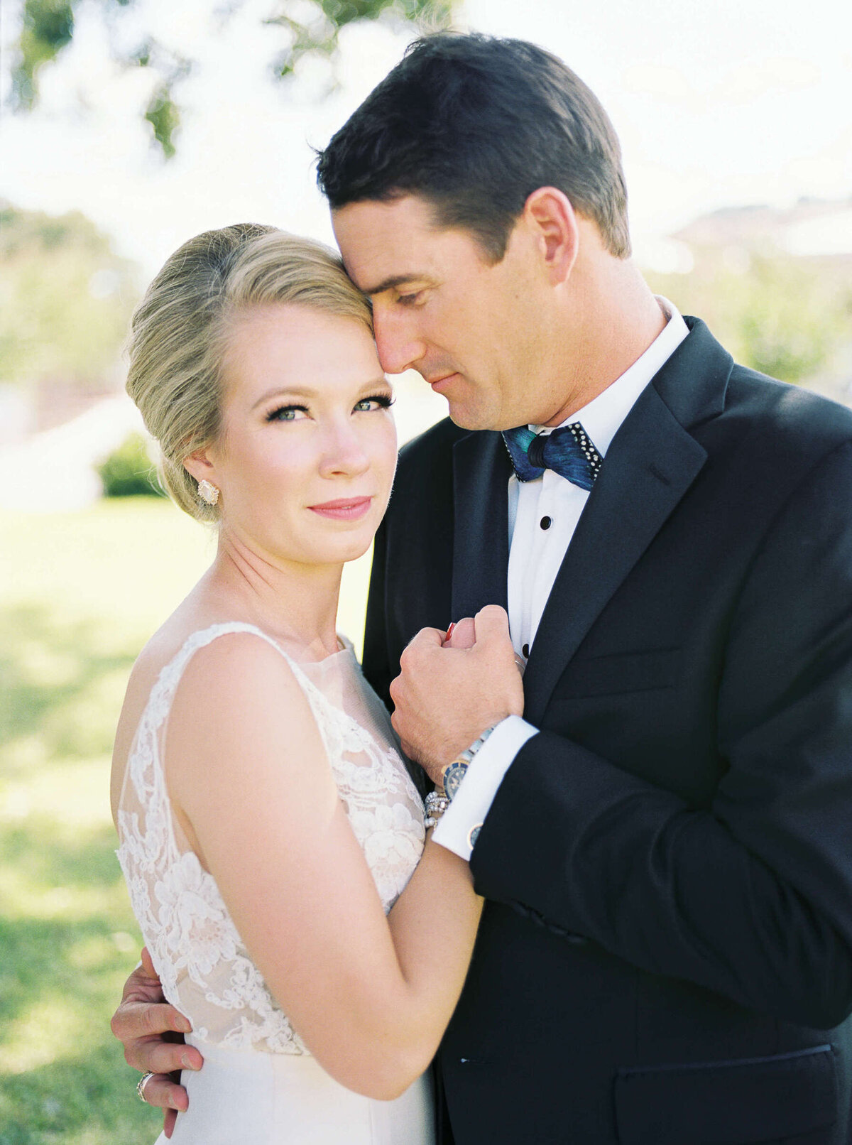 Elegant bride in Texas hill country looks at camera while her husband holds her