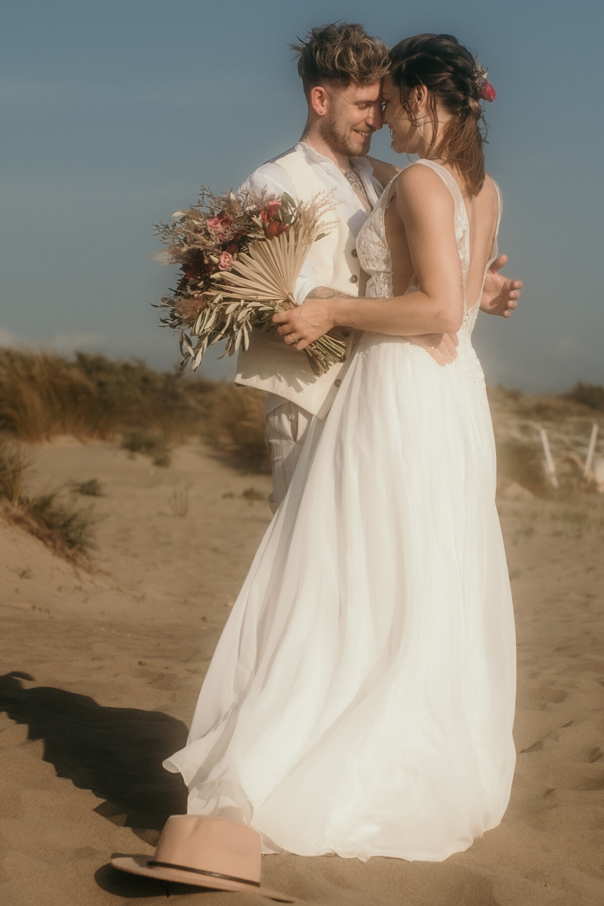 Die Stirnen aneinander gelehnt, steht das Hochzeitspaar in einer Umarmung am Strand.