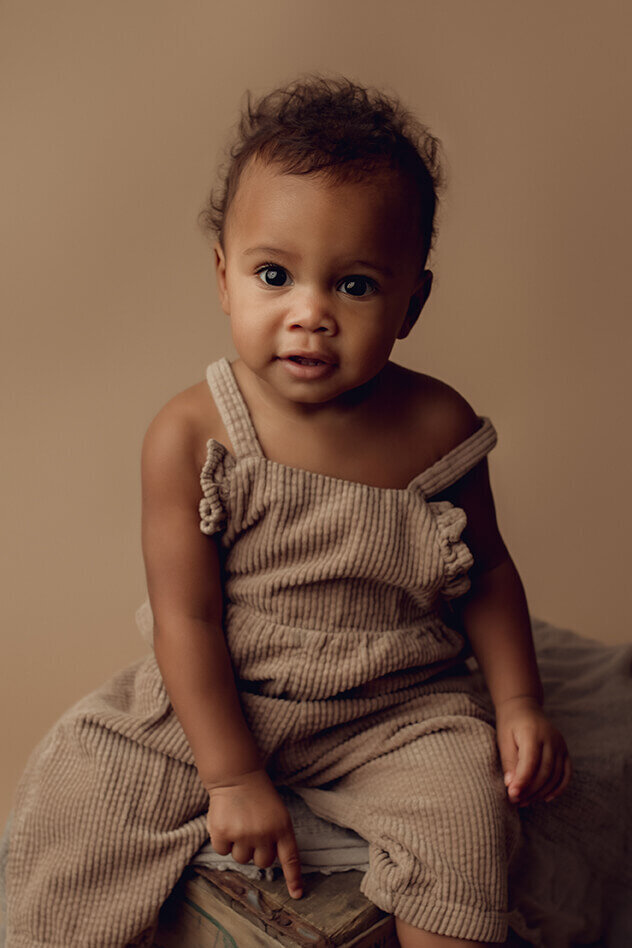 one year old girl in a brown jumper sitting on a crate in rochester ny lulu belle photography