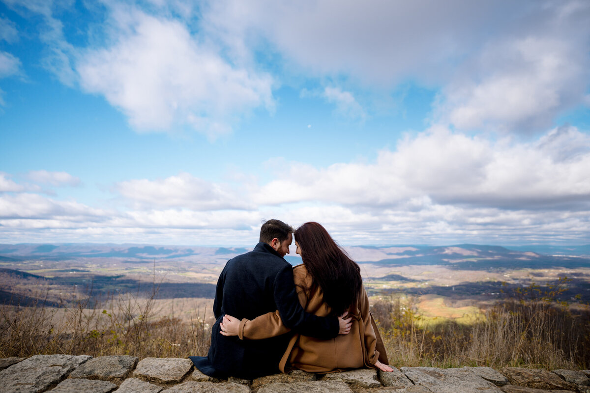 A couple sitting on a rock ledge with their arms around each other.