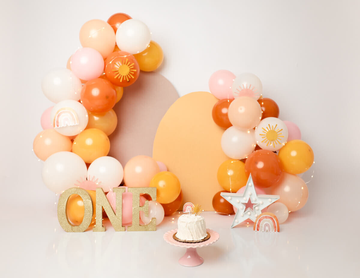 Baby girl celebrating her first birthday with a colorful balloon cake smash session.