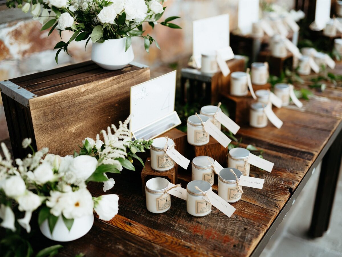 Closeup of candle wedding favors on farmhouse table with white and green bouquets at Hudson Valley wedding.