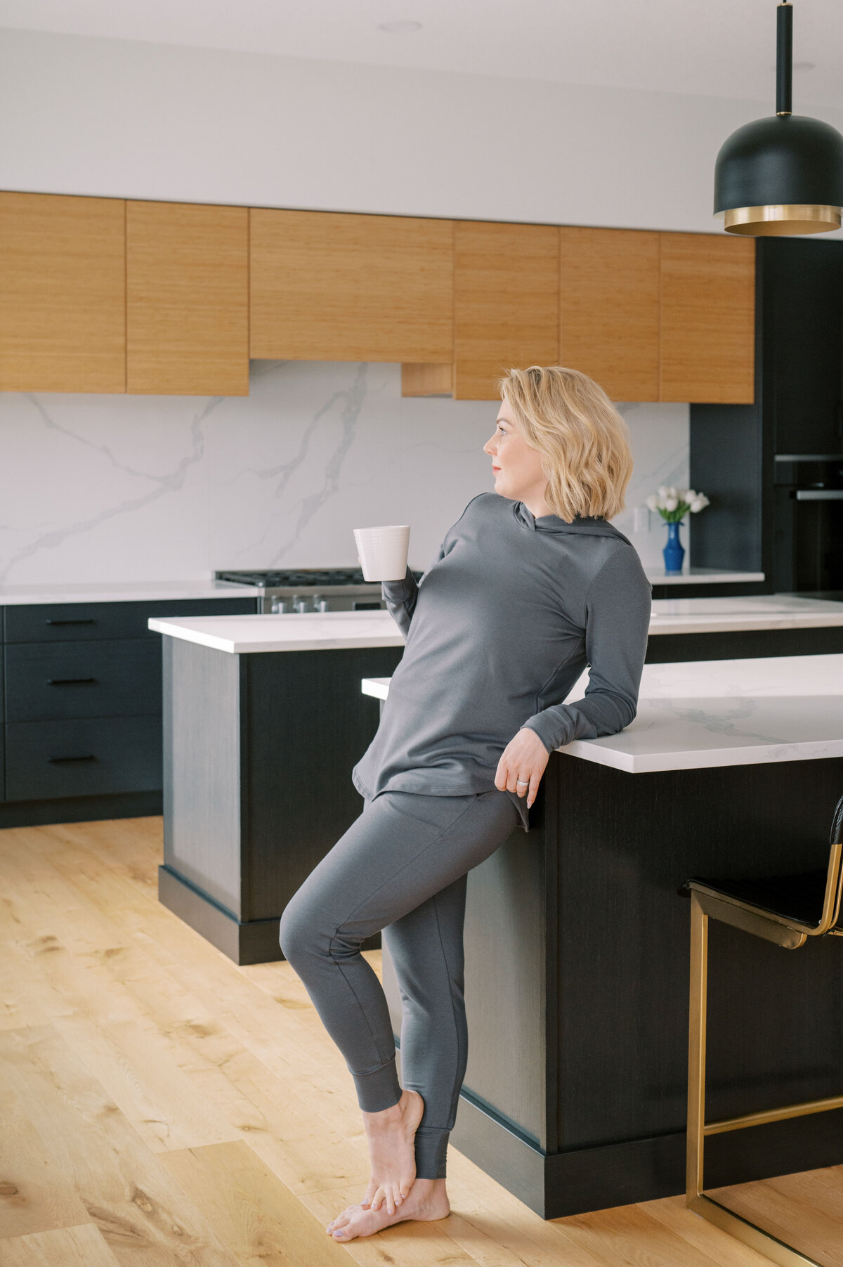 Woman wearing Lost in layers grey sweatsuit holding coffee mug in modern kitchen