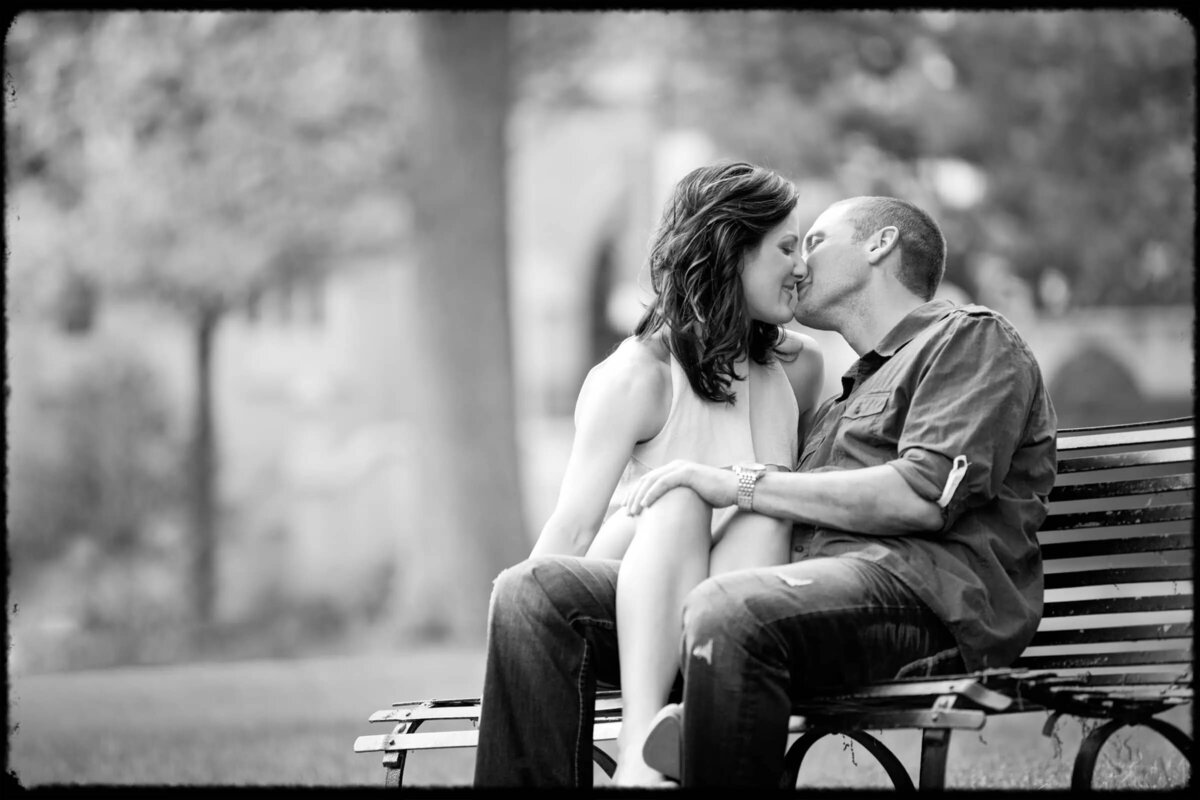 Monochrome image of a couple seated on a park bench, sharing a kiss amidst a serene park setting