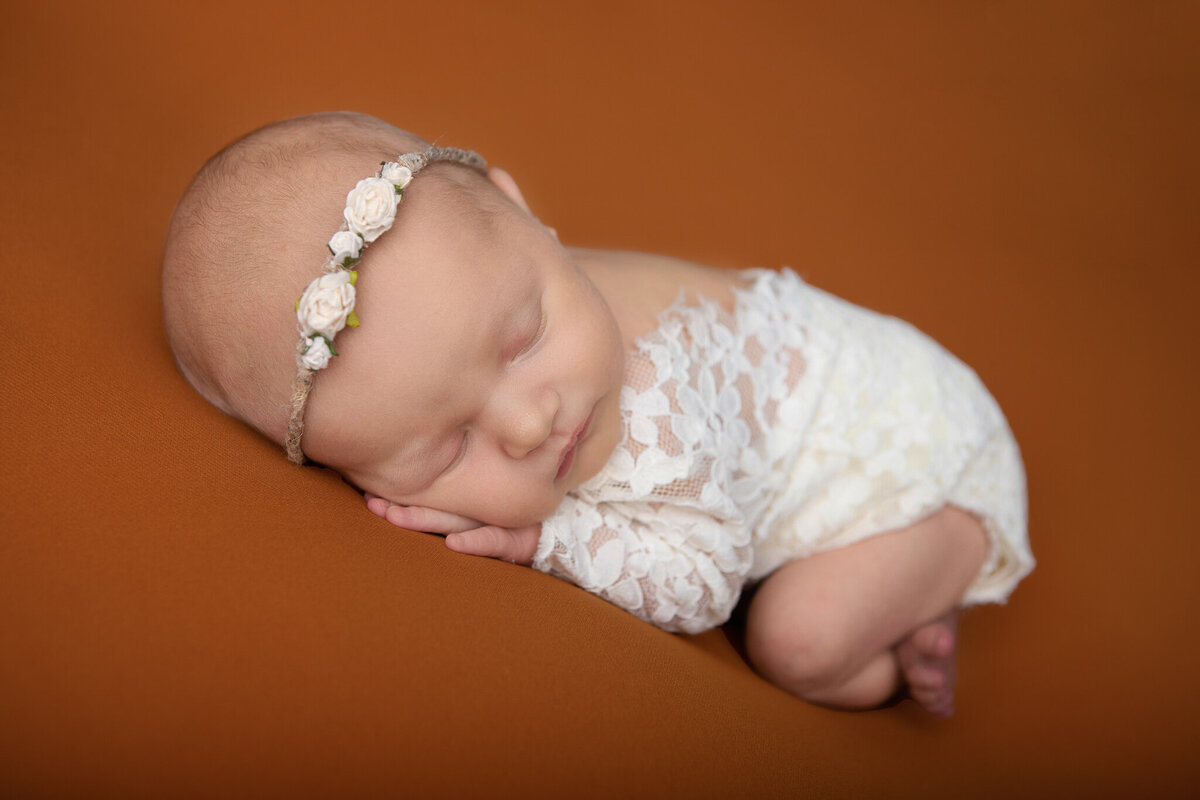 Studio chin up newborn pose in a lace onesie on an orange backdrop