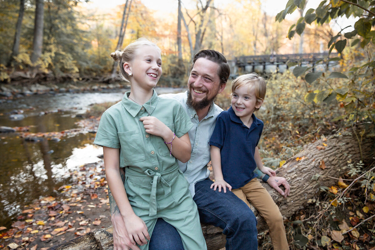 A father makes his kids giggle while sitting on a log in Jerusalem Mills in Kingsville, Maryland