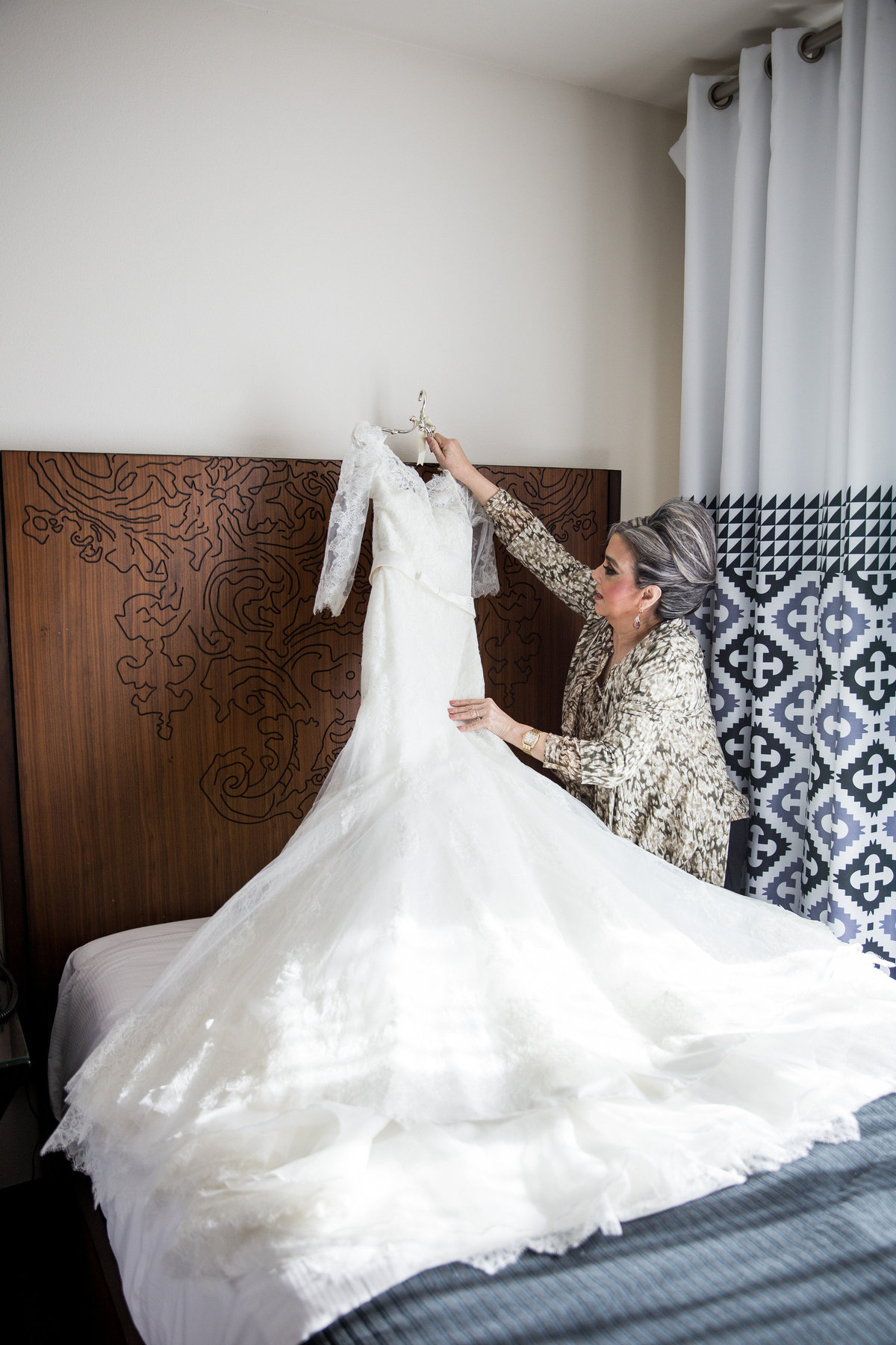 Mother of bride hangs wedding gown on bed during getting ready at Hotel Contessa in downtown San Antonio