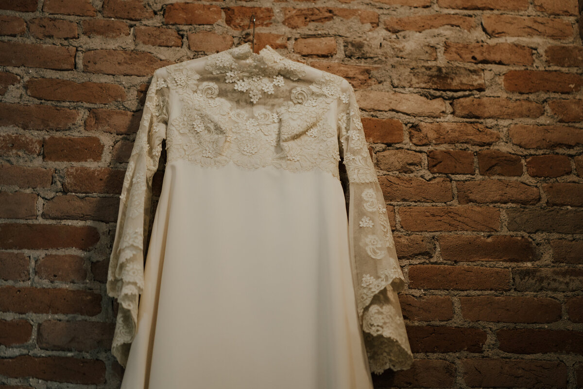 Heirloom wedding dress, with long sleeves of lace hangs on the brick wall of the interior of The Beaumont Hotel in Ouray, Colorado