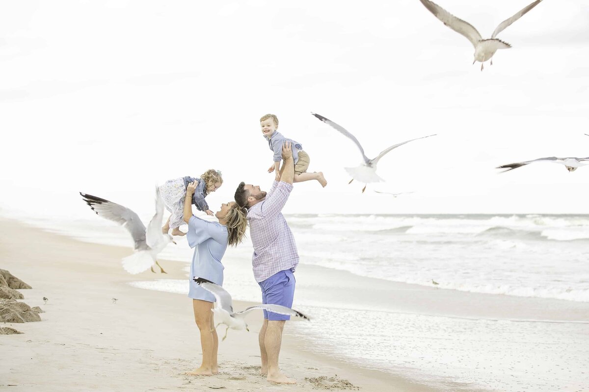 Parents standing back to back each lifting a child above their head on the beach