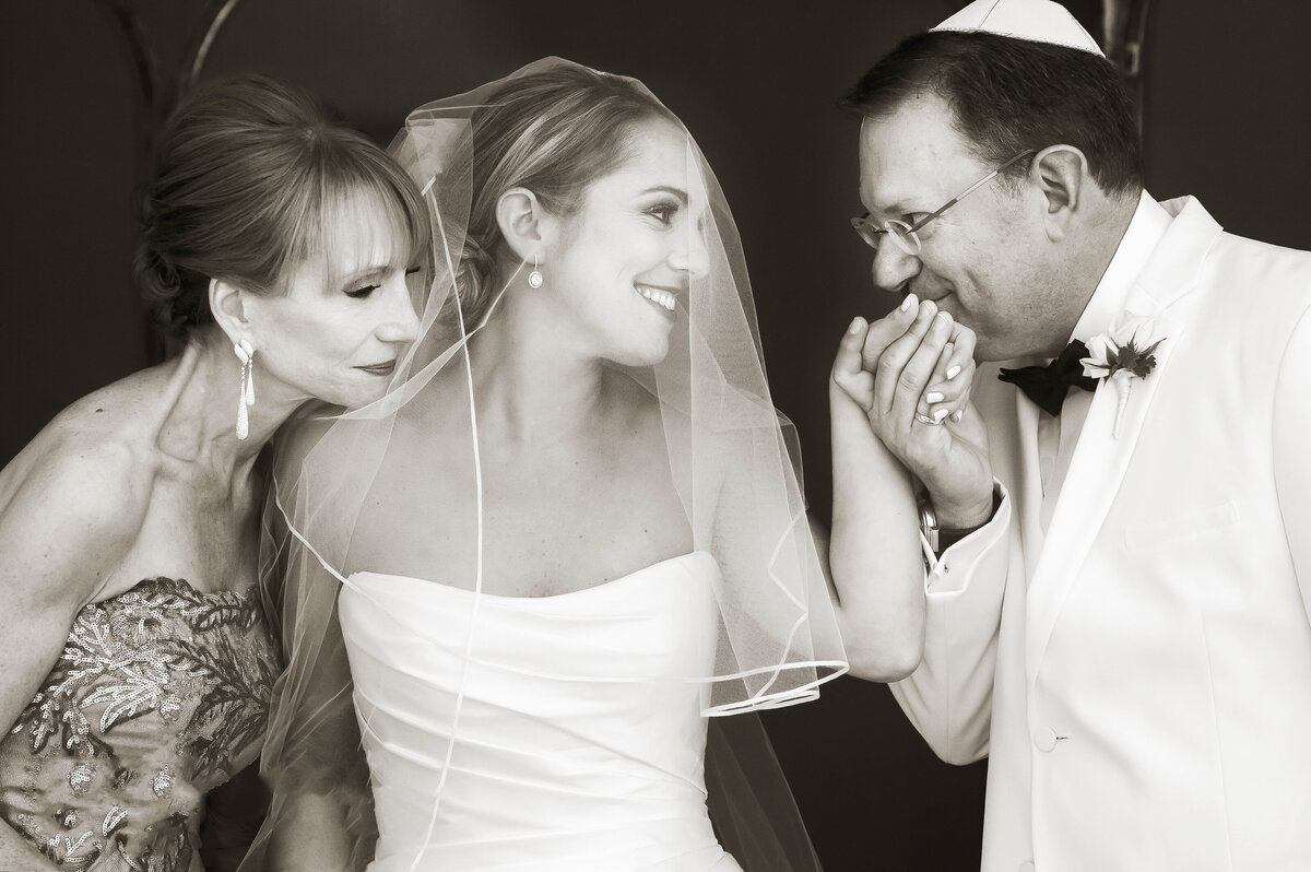 A person kissing a bride's hand with another person standing next to her.