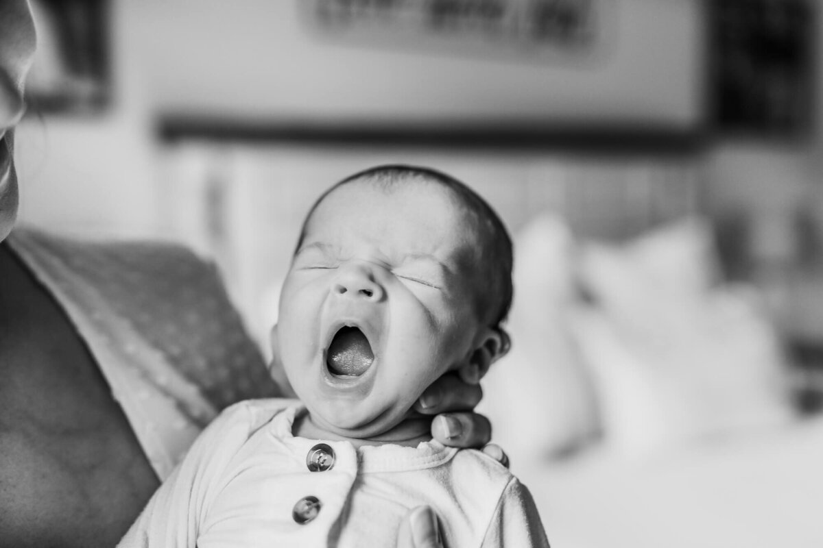 In home newborn session in Pearland, Texas of baby yawning while mom holds him.