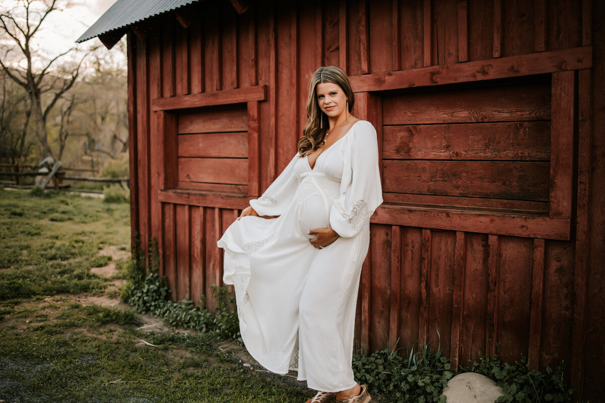 pregnant mom wears a long white dress in the fall for maternity photos in denver colorado