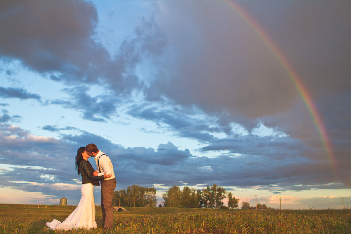 couple standing in a field with a rainbow