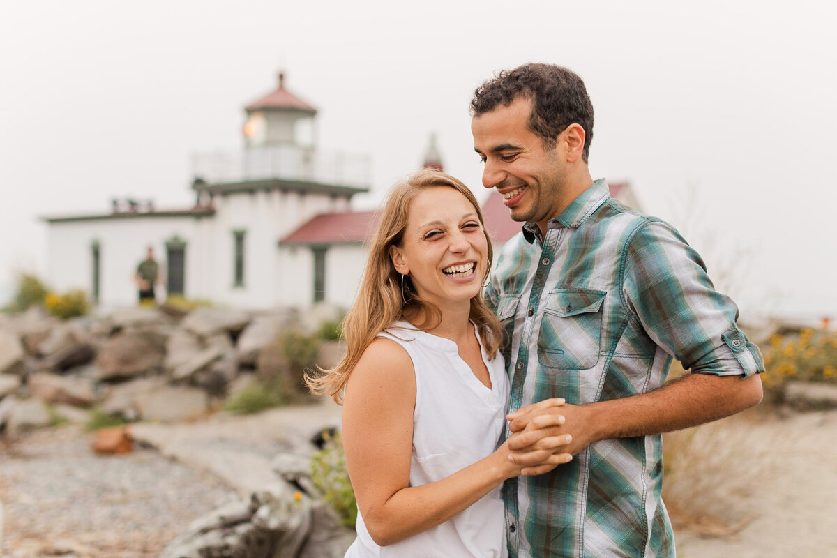 Fun and joyful engagement session at Puget Sounbd Beach Discovery Park in Seattle happy couple laughing in front of lighthouse candid photo by Joanna Monger Photography