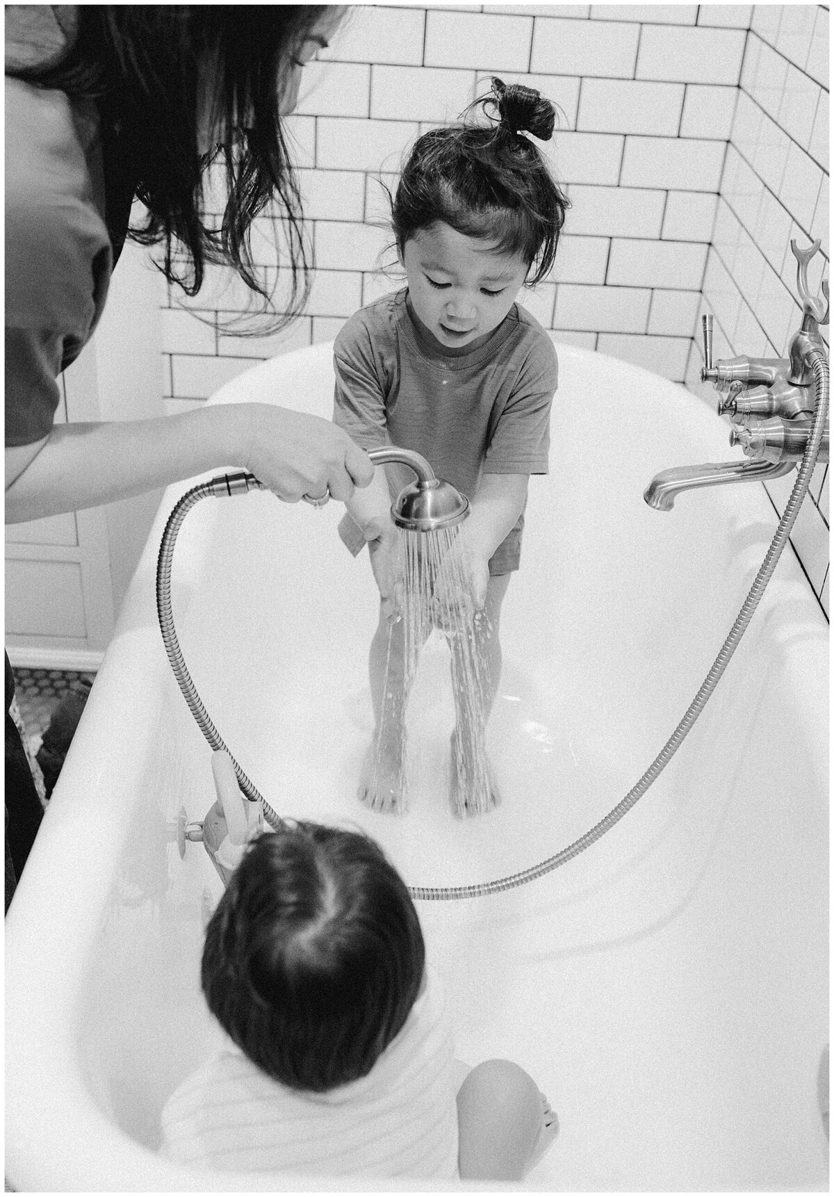 Two children in a bathtub as mother fills it with water