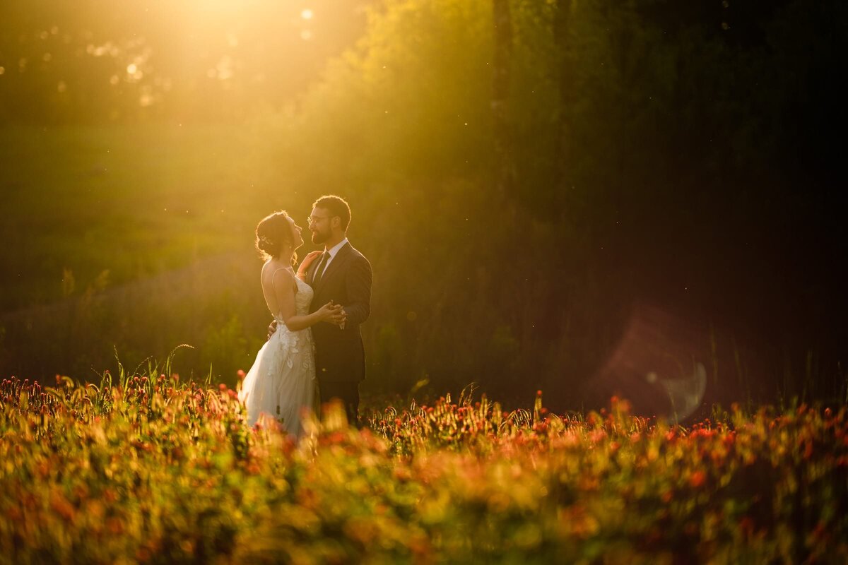 A bride and groom smiling in a field at sunset.